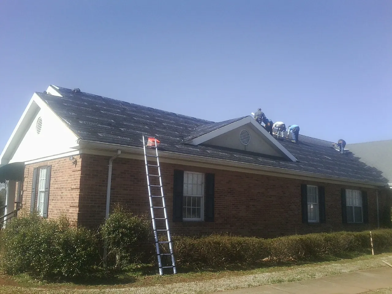 Crew tearing shingles off a brick ranch roof with a ladder set — Emergency Roof Repair work by our crew in Divide