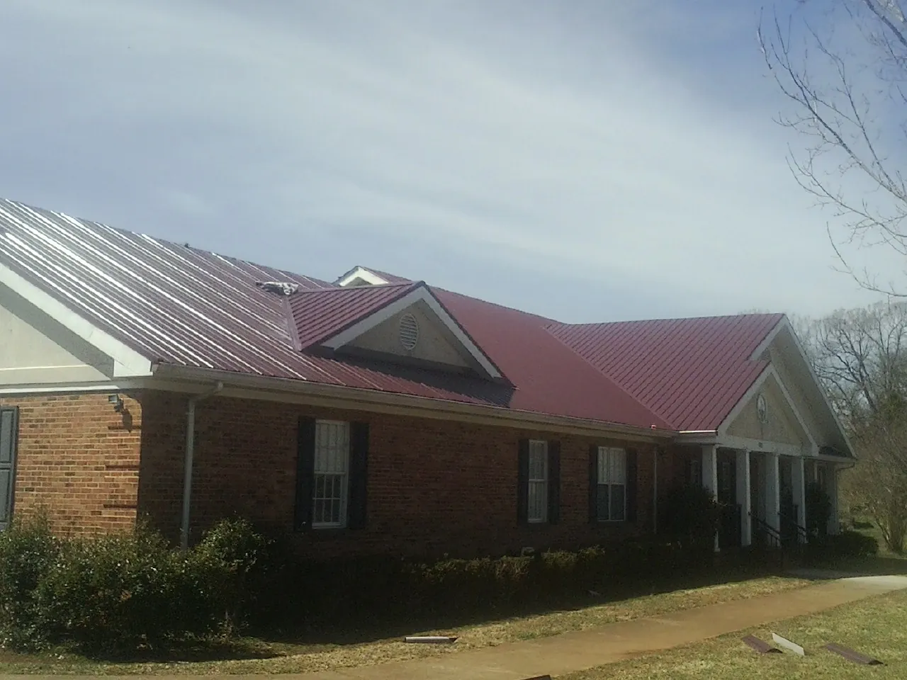 Red metal roof with gabled entries on a long brick building, from a Hail Damage Roof Repair job in Divide