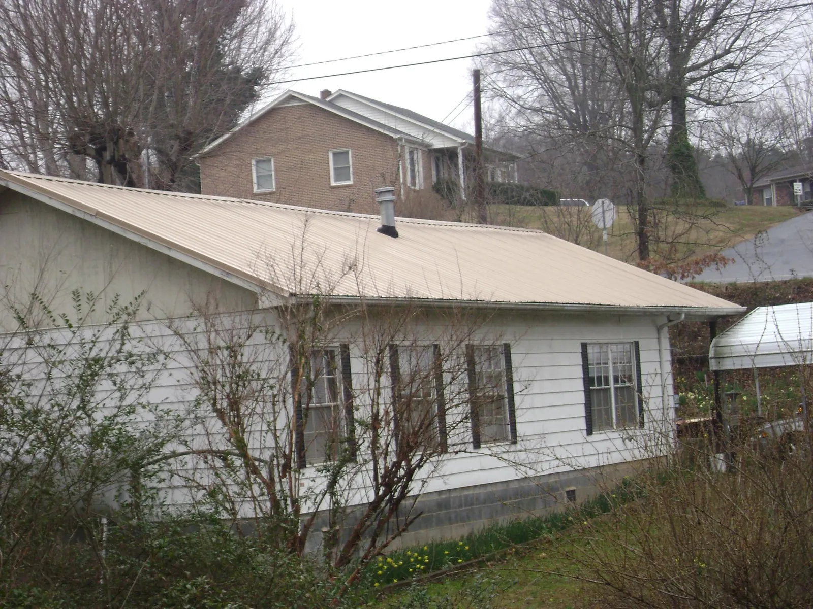 Tan metal roof on a white sided house set into a hillside — Commercial Roofing by Roofing Brothers in Divide
