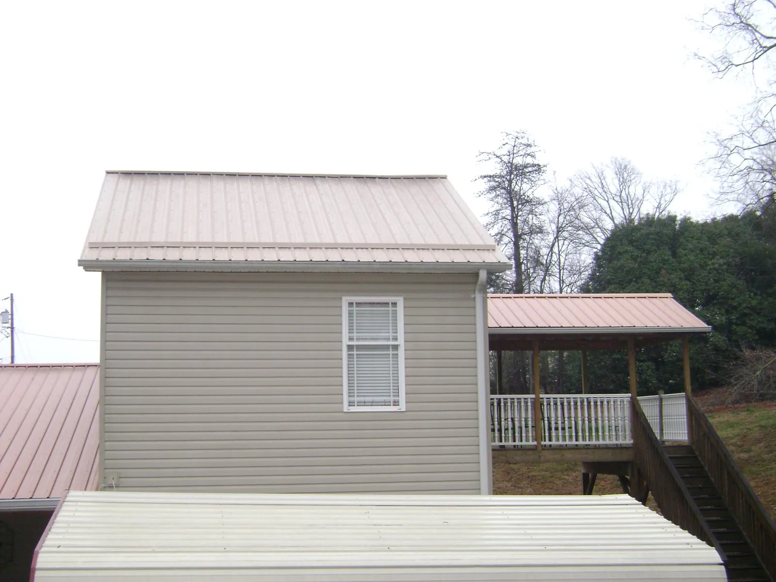 Tan metal roofs on a two story addition and attached porch, from a Roof Replacement job in Divide